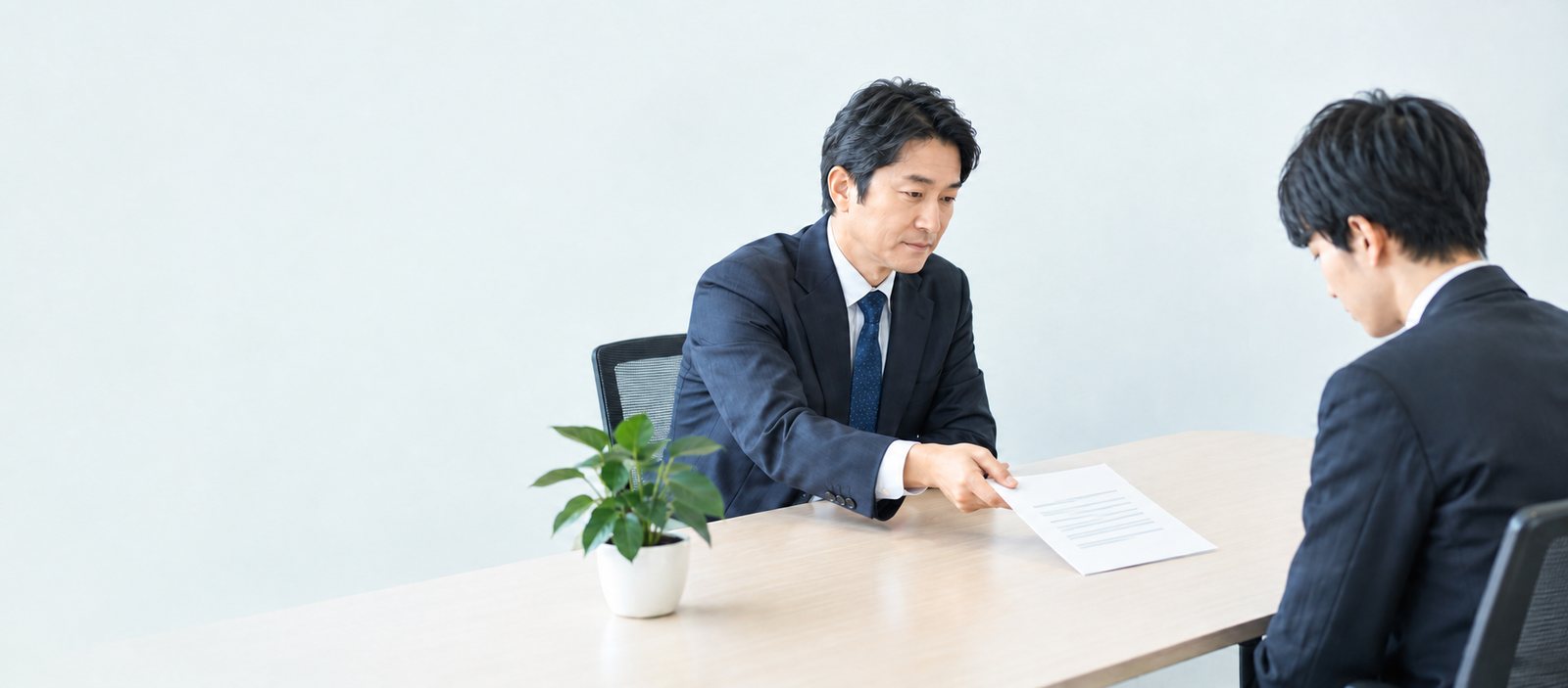 上司が評価シートを差し出し、部下がうつむいて見ている面談の場面（イメージ）